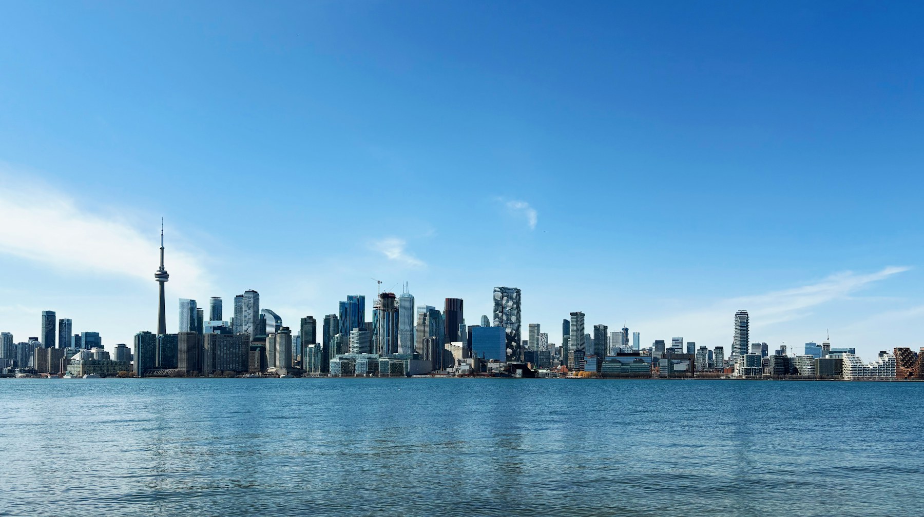 Toronto skyline and CN Tower under a bright blue sky, viewed across the harbour